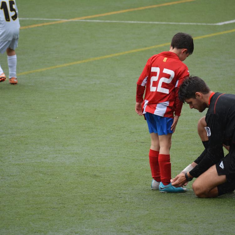 Illustrasjonsbilde av en trener som knyter fotballskoene til et barn på banen. Foto: Unsplash.com/Adria Crehuet Cano